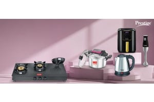 Prestige kitchen appliances including black gas stove, silver pressure cooker, black air fryer, electric kettle, and hand blender on a pink background.